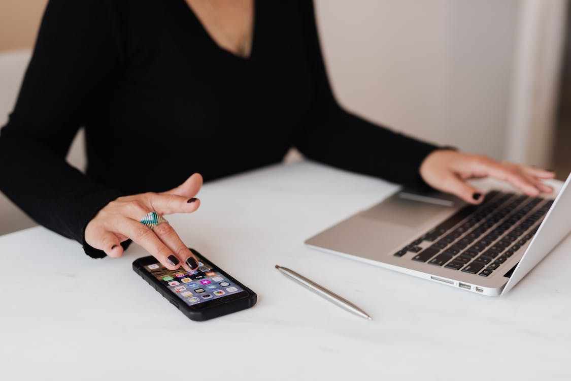 A woman with laptop scrolling through the mobile phone - Koofr blog