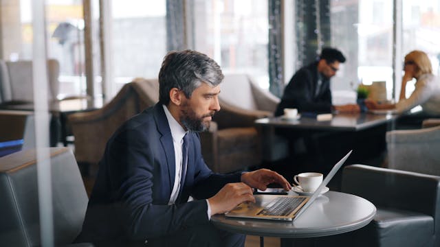 A man in a suit sitting at a table with a laptop