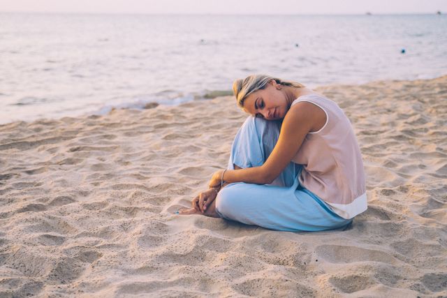 A woman sits peacefully on a beach with closed eyes, embracing serene ocean vibes