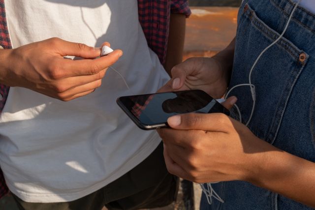 Close-up of teenagers sharing music on a smartphone outdoors with earphones