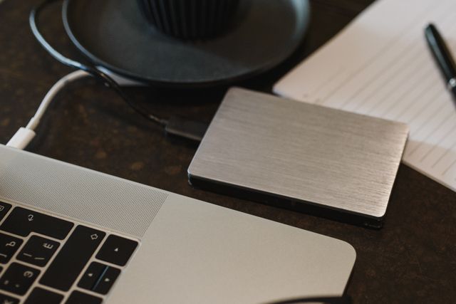 Closeup of an external hard drive connected to a laptop with a USB cable on a desk