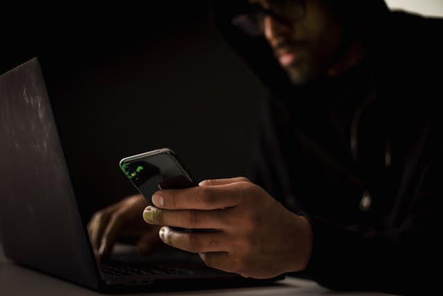 Crop hacker with smartphone typing on laptop in dark room.jpg