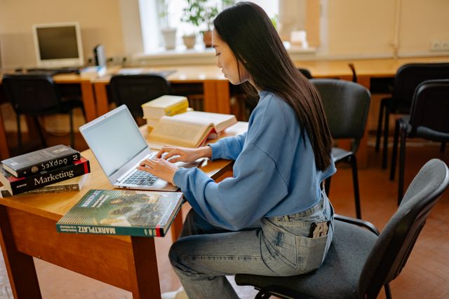 Focused woman typing on laptop, surrounded by books in a cozy study spot.jpg
