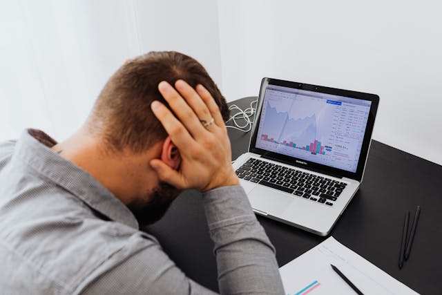 Man with Laptop on Desk Terrified by Stock Market Chart