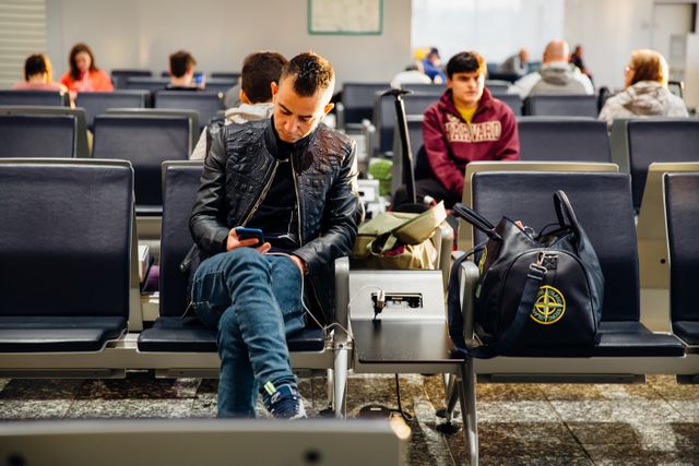 People sitting in an airport lounge, focused on smartphones and waiting for flights