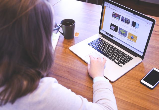 Person browsing the web on a MacBook at a wooden desk with a smartphone