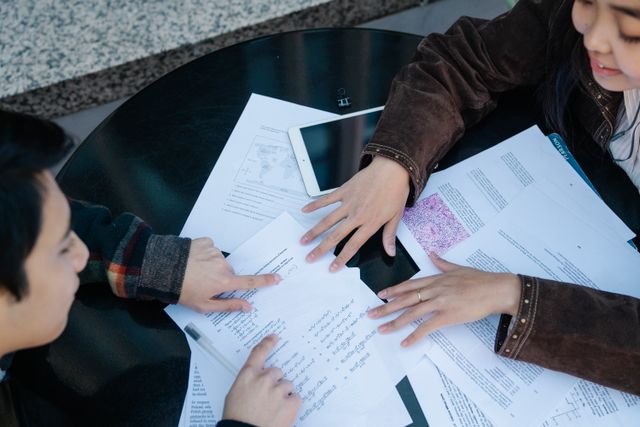 Two students discuss and study together with papers on a table, showcasing collaboration and education