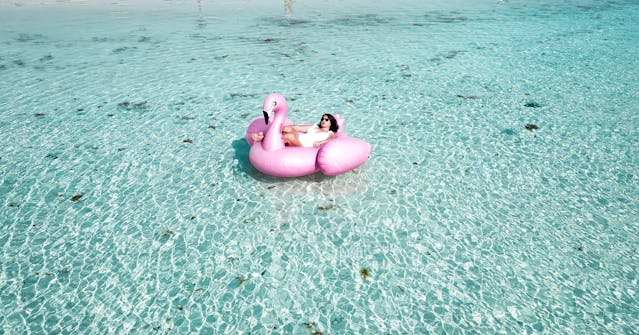 Woman Lying on Pink Flamingo Bouy on Body of Water